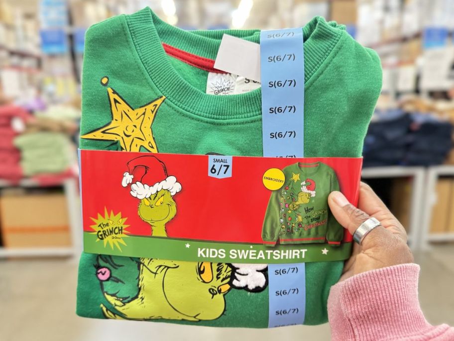 a womans hand holding a kids grinch sweatshirt