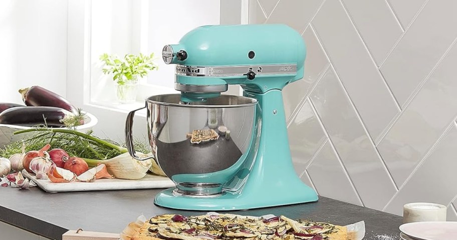 an aqua blue KitchenAid stand mixer with a silver bowl on a counter, serving board of food in front of it