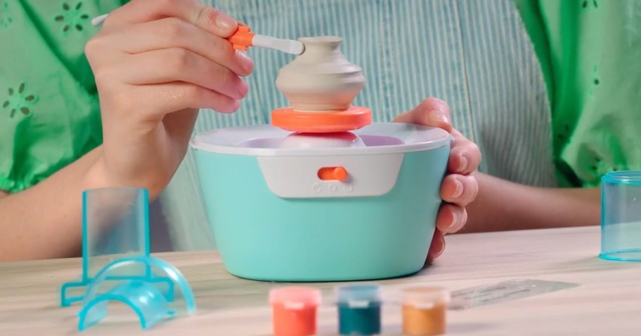 a kid using a mini pottery wheel machine to make a mini vase