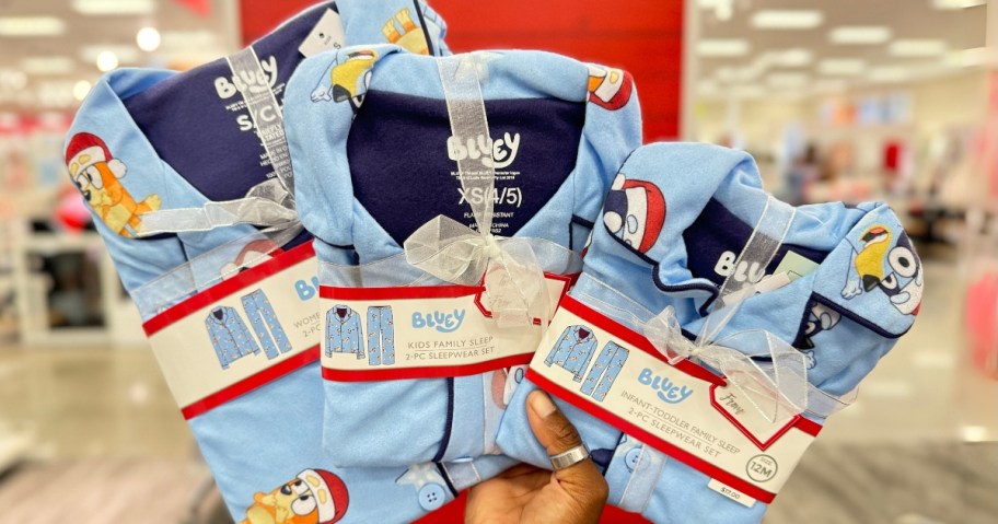 hand holding adult and kids sets of blue color Bluey family matching pajamas in Target