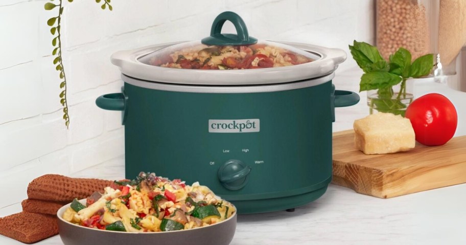 a dark green Crock pot with food in it, bowl of food in front of it, sitting on a counter