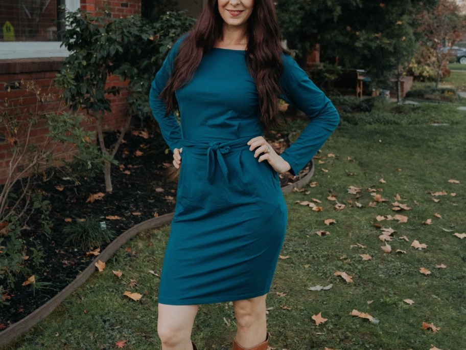 woman wearing a teal green long sleeve tie waist knee length dress standing outside posing for the camera