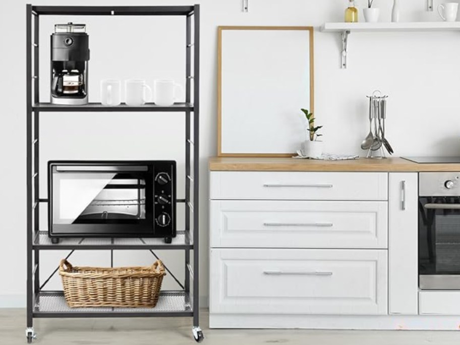 a black adjustable folding metal shelf with wheels in a kitchen holding a coffee maker, microwave, and basket with other kitchen items