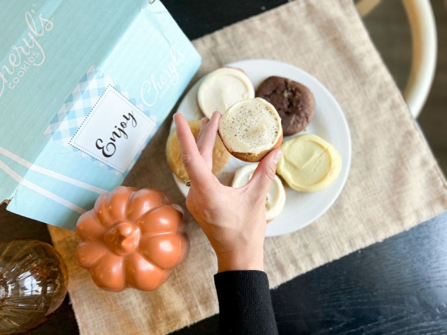 A person holding a cookie in front of Hip2Save’s Cheryl’s Experience Box