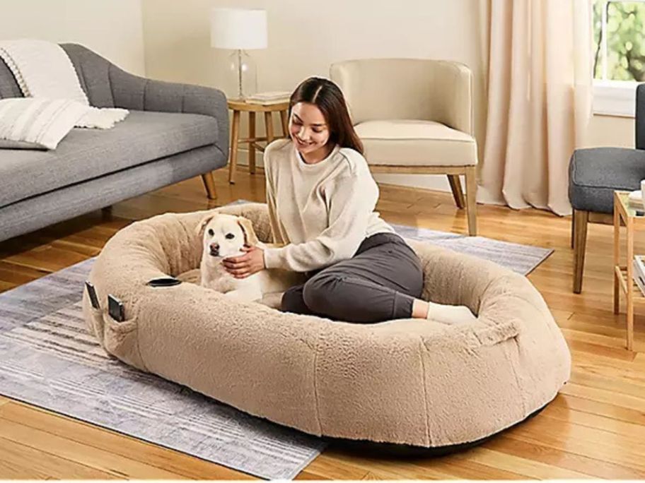 woman in a human sized pet bed with her dog