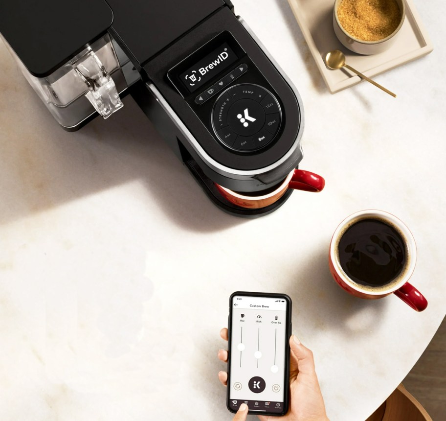 person using phone to brew cup of coffee from keurig