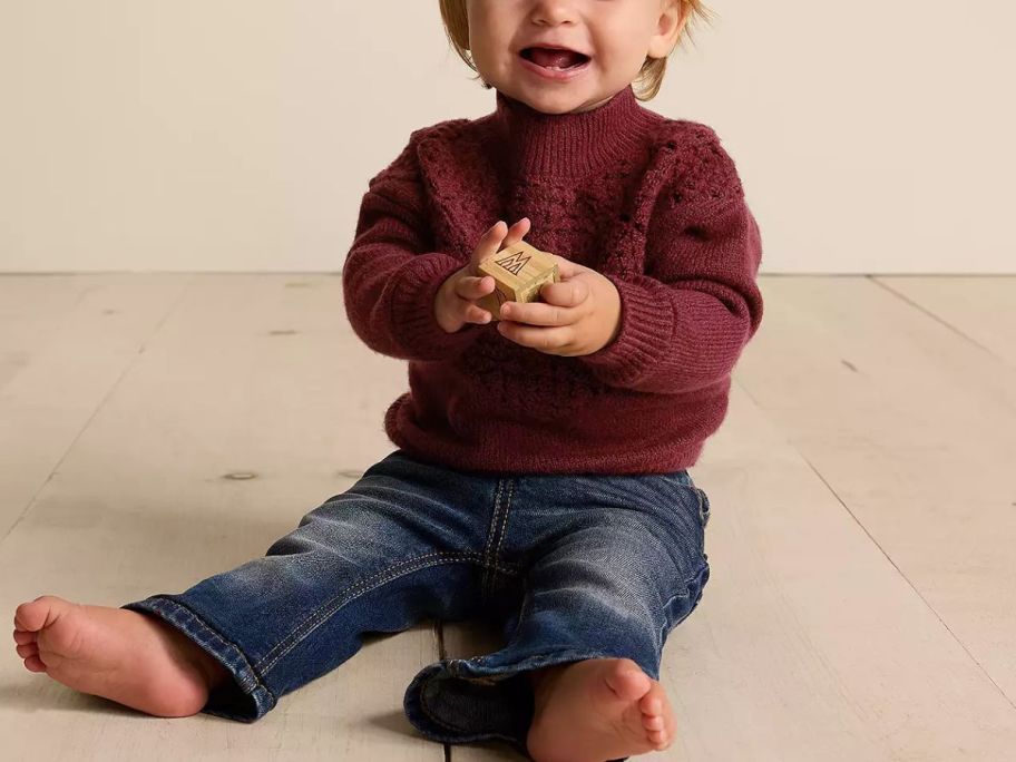 A baby wearing a Little Co. Sweater and jeans