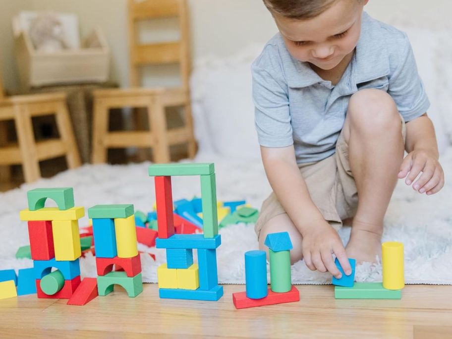 kid playing with Melissa & Doug Wooden Building Blocks Set on floor