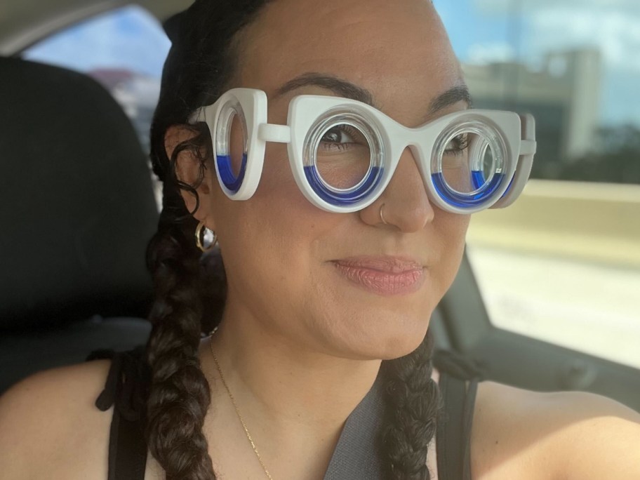 woman wearing white and blue motion sickness glasses that have lenses on her eyes and the sides of her face, she is riding in a car