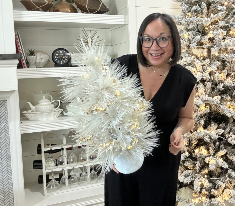 A woman holding up a small christmas tree decorated with gold lear garland from Walmart