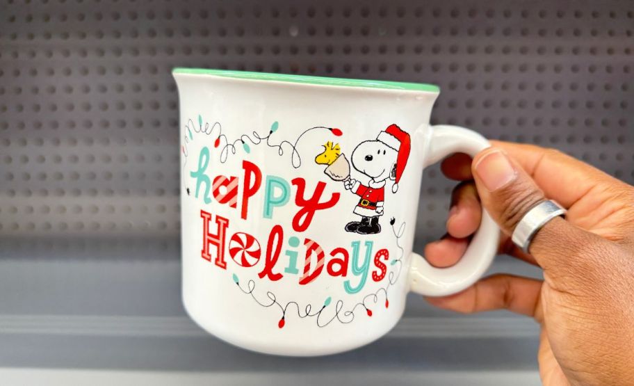 a womans hand holding a snoopy holiday mug