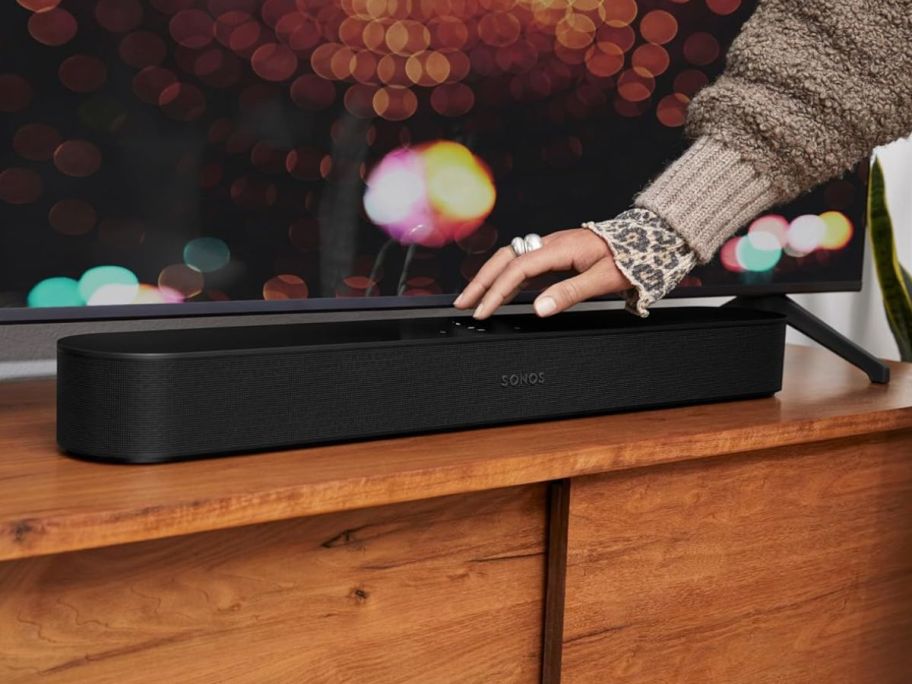 Sonos Beam Soundbar in front a TV with a woman's hand resting on it