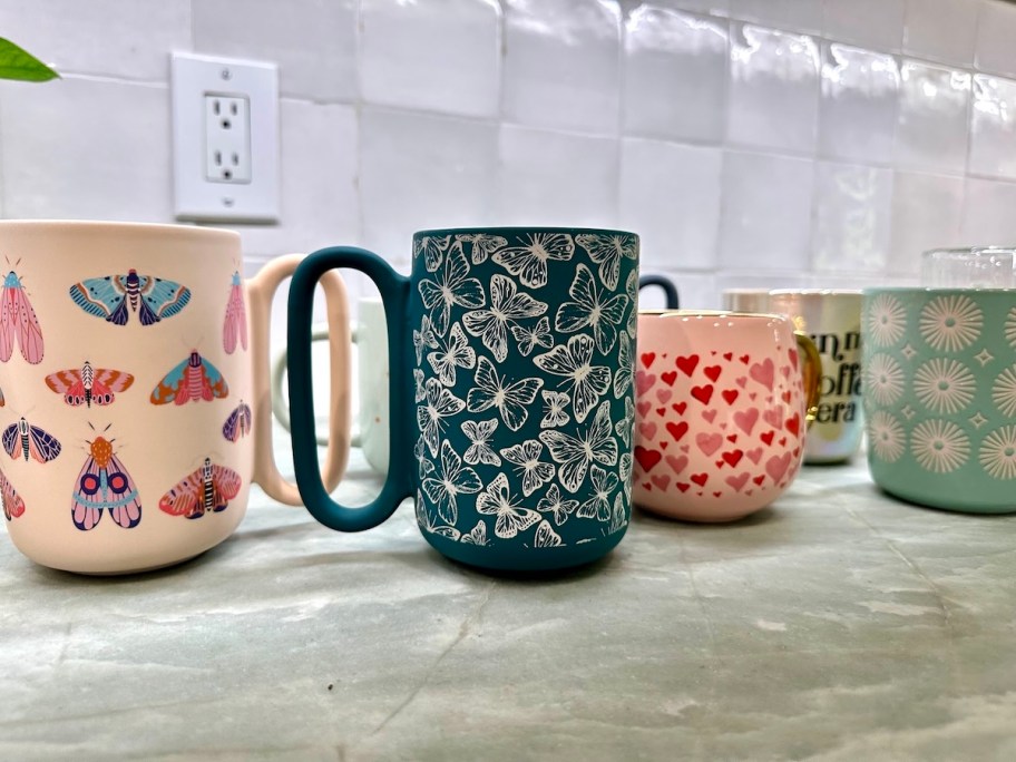 row of eclectic coffee mugs on green kitchen countertop