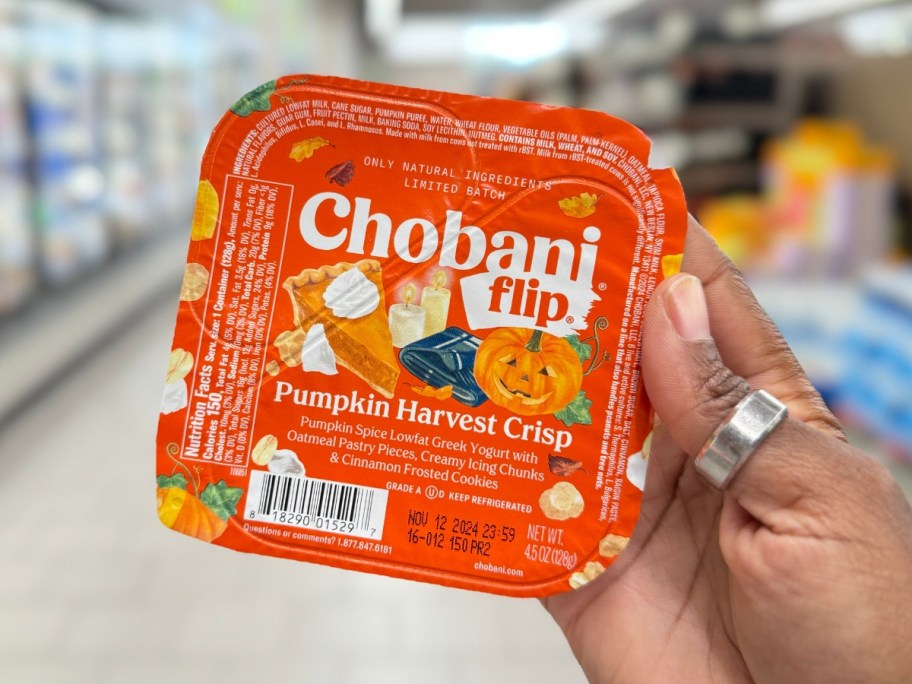 hand holding an orange and white container of Chobani Flip Pumpkin Harvest Crisp flavor