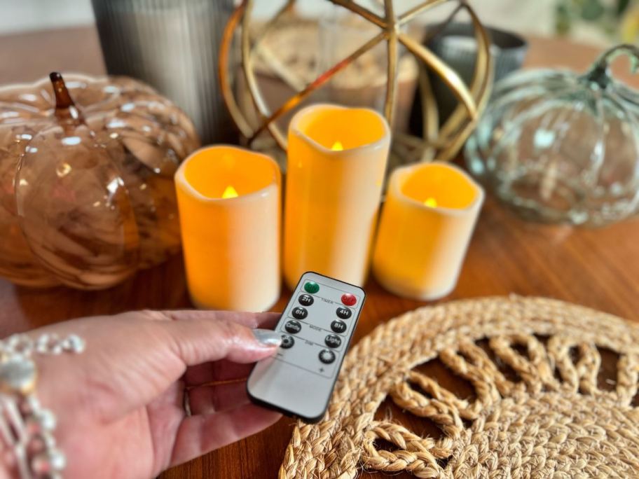 hand holding remote in front of flameless candles on dining table