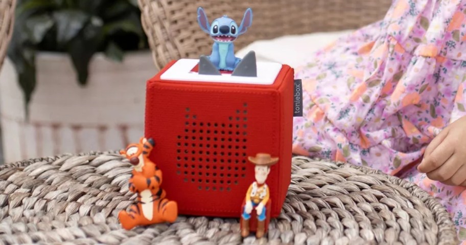 a red Toniebox audio player with a Disney Stich figure on top and a Tigger and Woody figure beside it, sitting on a wicker table