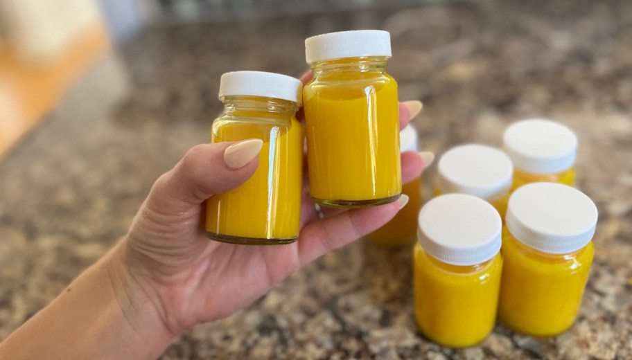 hand holding ginger turmeric shots in glass shot bottles