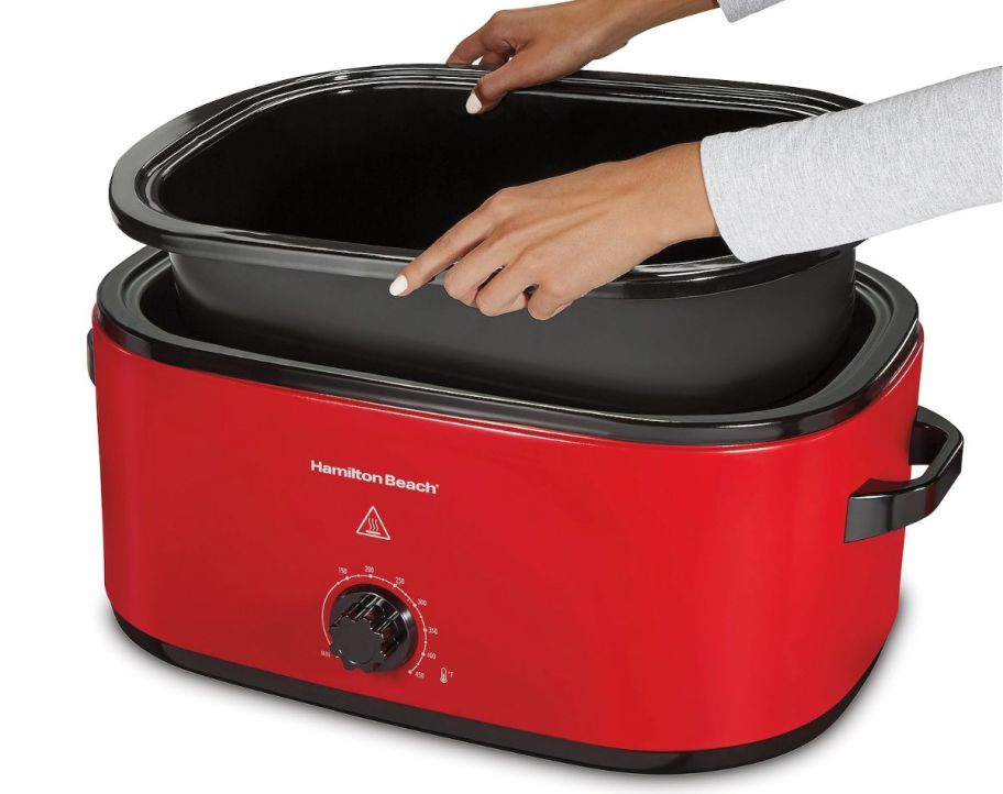 a womans hands taking the inner pan out of a red electric roaster