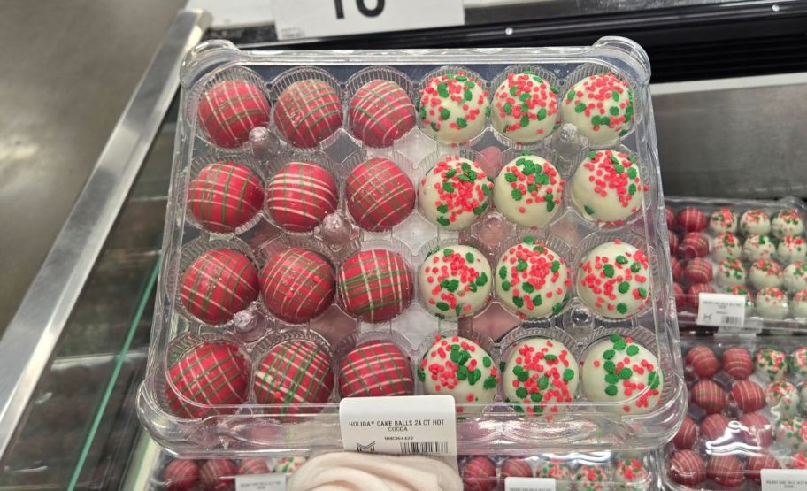 a womans hand holding a container of holiday cake balls