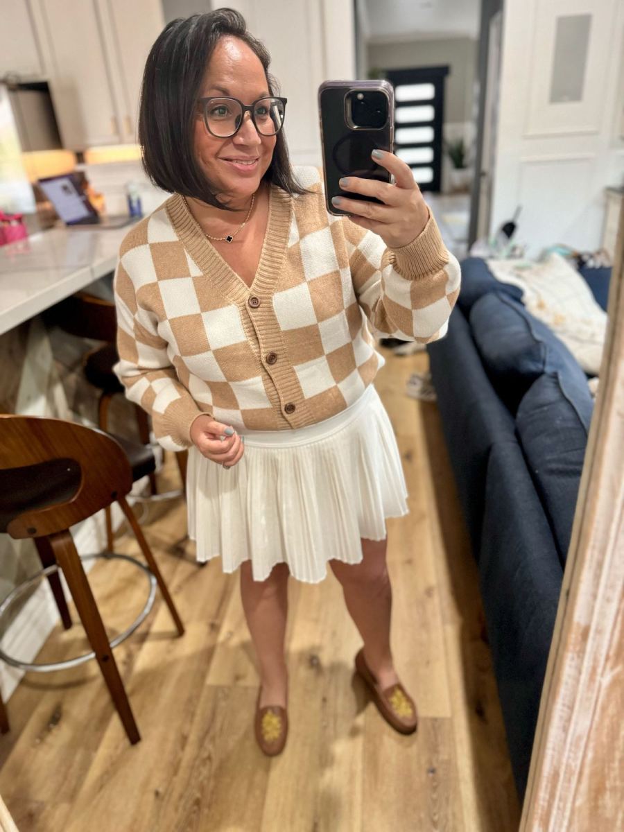 woman taking selfie in mirror wearing white skirt and checked sweater