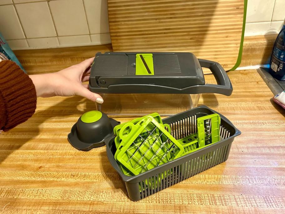 person holding veggie chopper with basked of accessories next to it