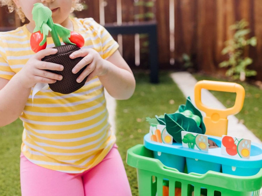 child holding up a pretend vegetable plant from the melissa & doug vegetable garden playset