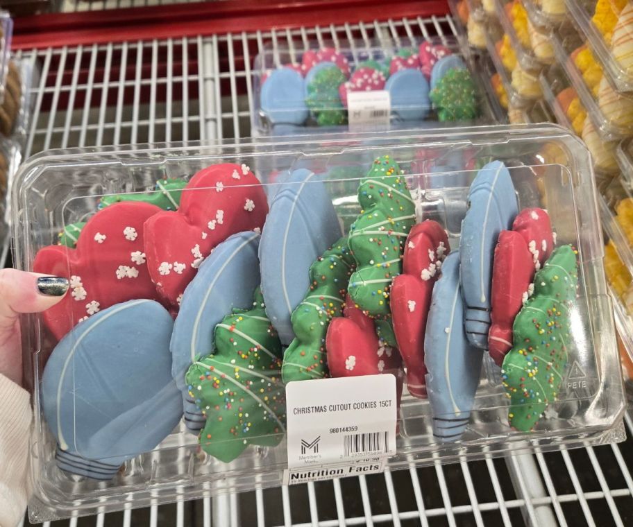 a womans hand holding a container of cutout cookies