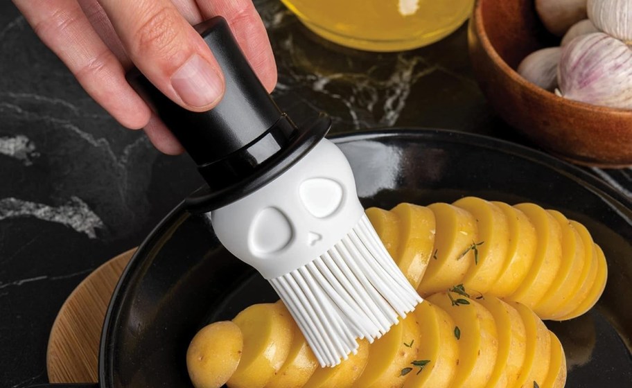 hand holding basting brush over potatoes on a plate