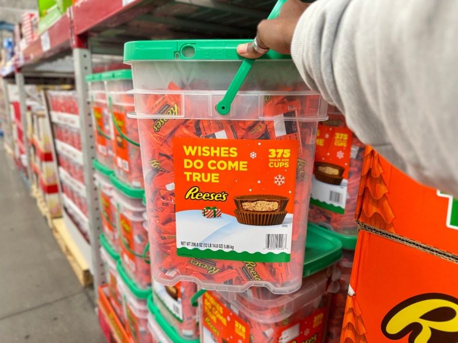 hand holding a large clear bucket with a lid filled with Reese's Peanut Butter Cups