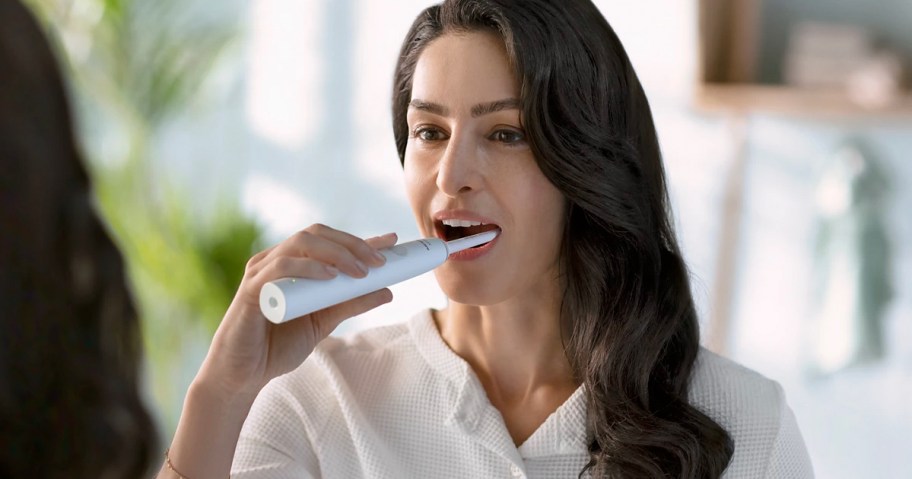 woman using white sonic care toothbrush 