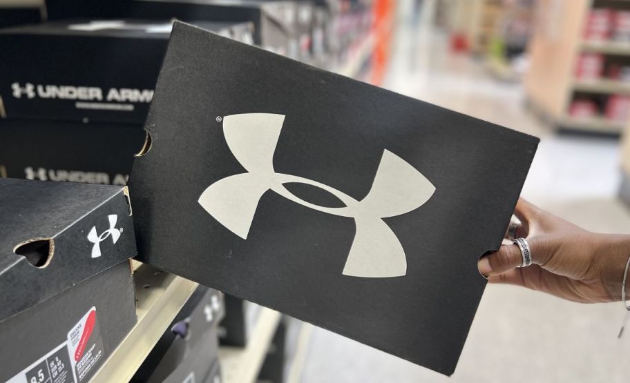 a womans hand grabbing an under armour shoebox from a store shelf