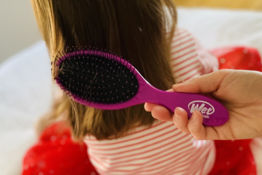 hand holding purple wet brush near girls hair