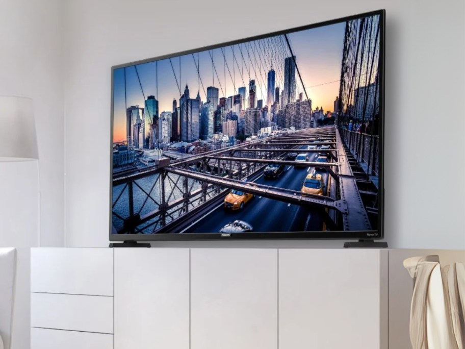 a large flat screen TV on a wall above a white cabinet, city landscape picture on the TV