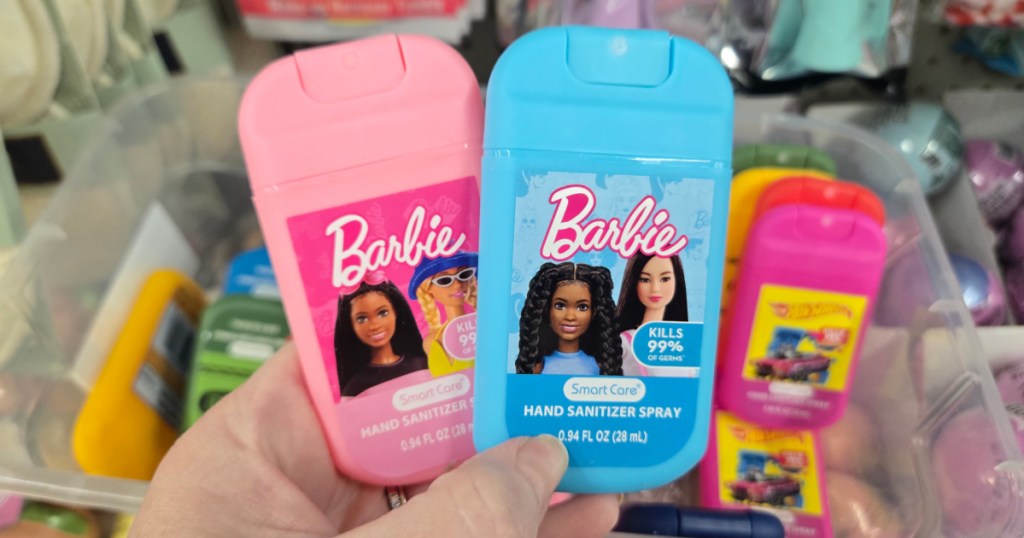 Woman holding up blue and pink Barbie kids hand sanitizer sprays inside Dollar tree