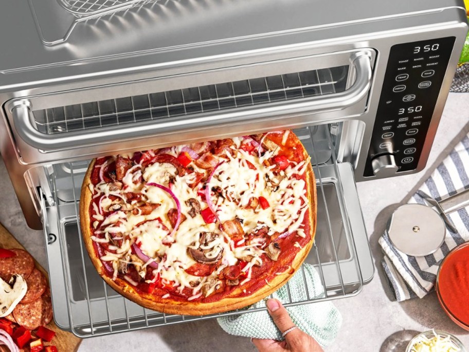 person taking pizza out of countertop oven