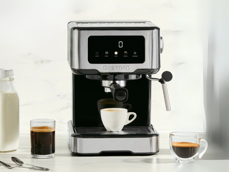 a silver and black espresso machine on a kitchen counter, cup of espresso in the maker, milk and other cups of coffee around it