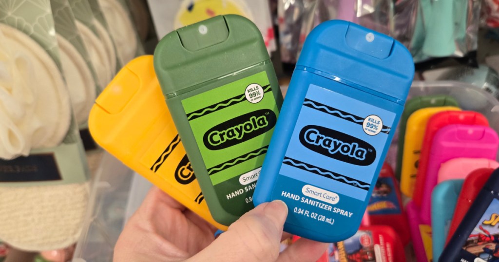 Woman holding up blue green and yellow Crayola hand sanitizer sprays inside Dollar tree store