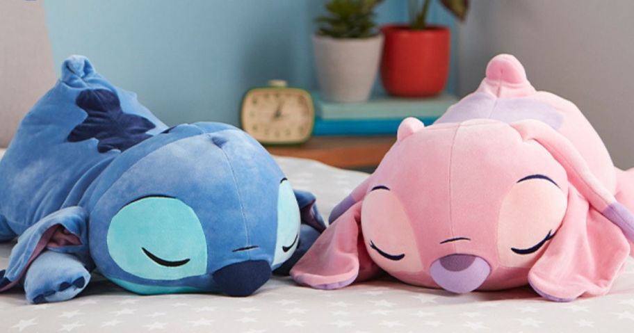 A Disney Cuddleez sleeping stitch and angel pillow on a bed