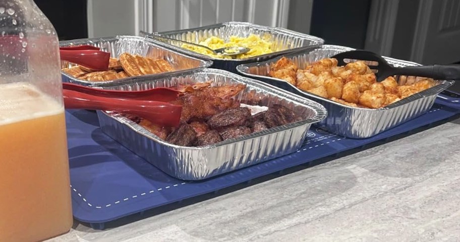 multiple aluminum pans filled with food on top of a blue warming mat