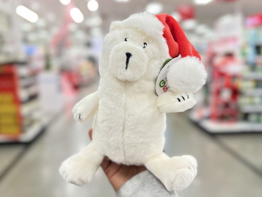 a womans hand holding a gigglescape plush bear in a red santa hat