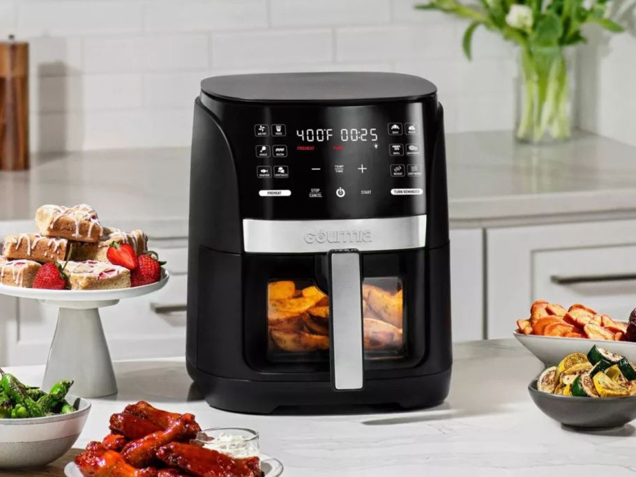 a black Gourmia 6-Quart Window Air Fryer on a kitchen counter with food around it