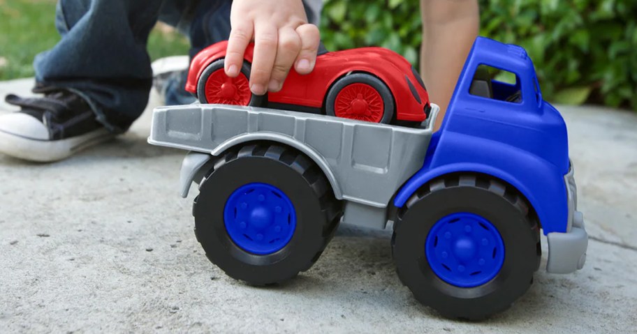 child playing with a grey and blue flat bed truck with a red race car on top