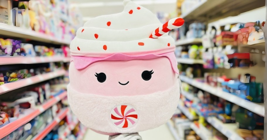 hand holding a large Squishmallow plush that is pink, white and red and looks like a big cup of hot cocoa