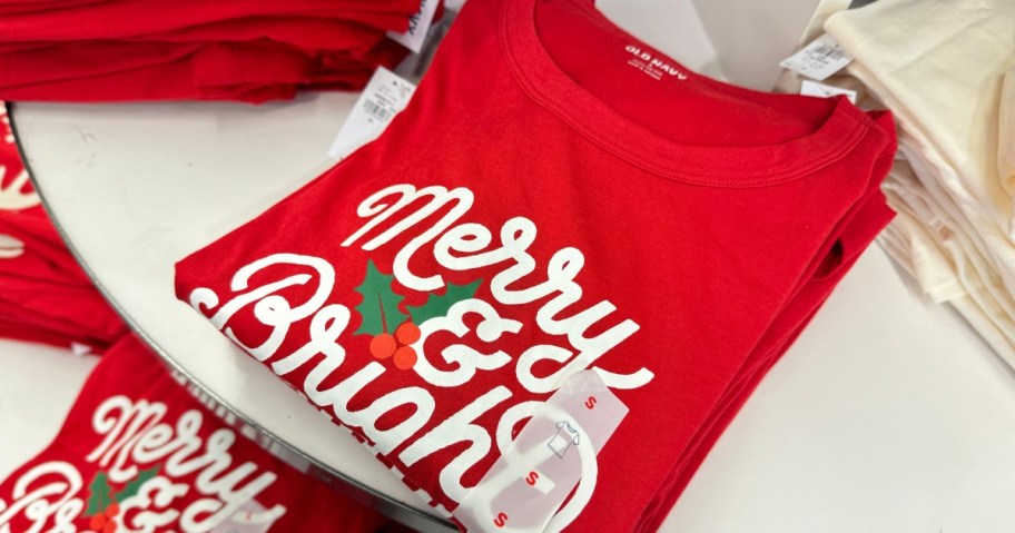 a red t-shirt that says "Merry & Bright" on a clothing display 