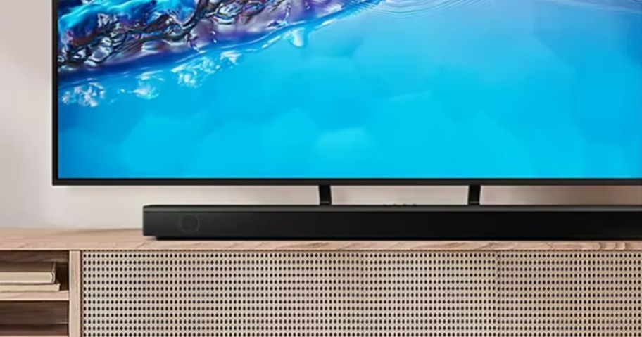 a large TV with a black soundbar sitting in front of it on a TV stand