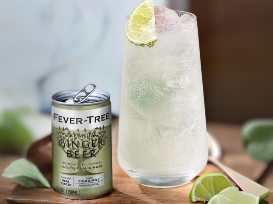 a small green can of Fever Tree Ginger Beer next to a glass with a mixed drink it in and some lime wedges