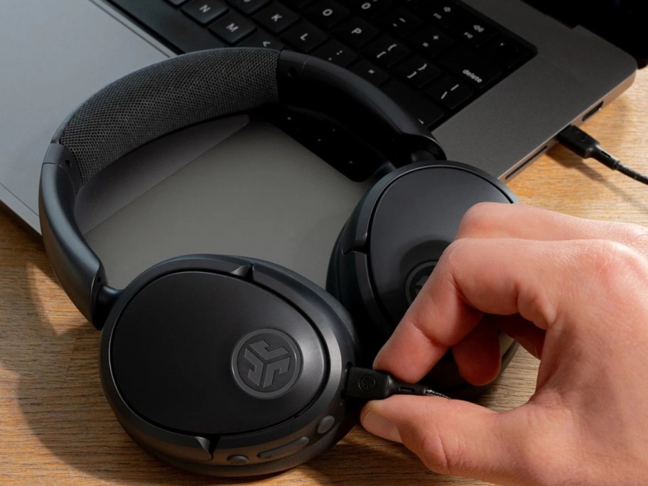 a pair of black Jlab wireless headphones with a person plugging them in to be charged