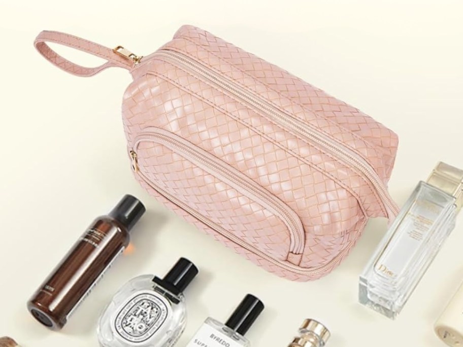 a pink faux leather makeup bag with several onlinepartments, beauty items laying in front of it