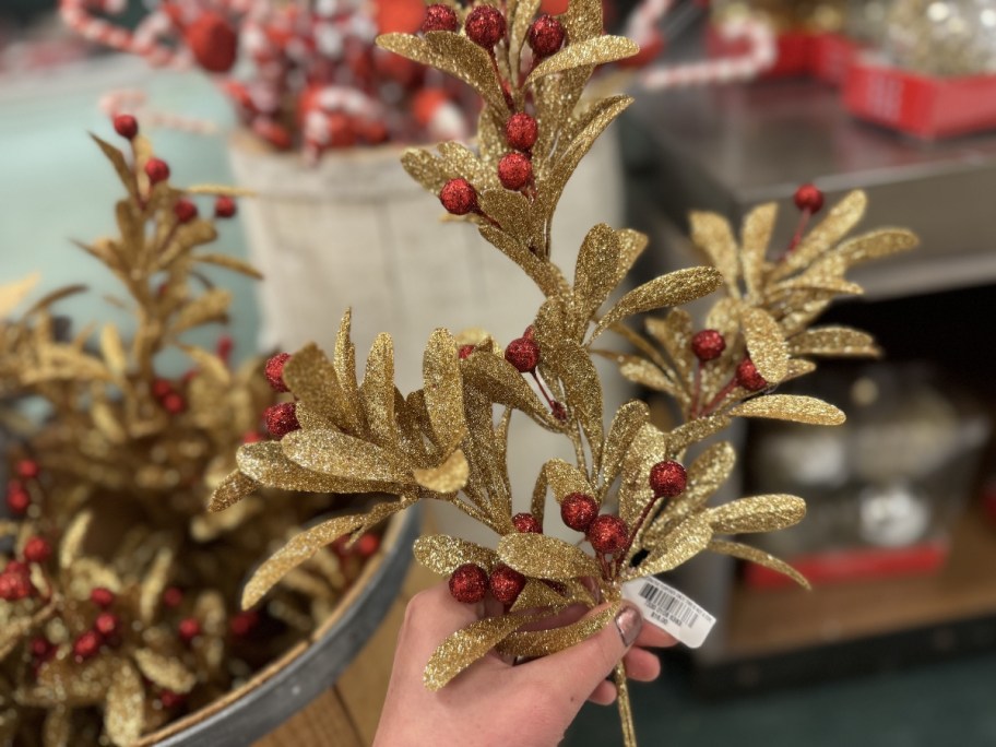 hand holding a gold glitter and red berry Christmas decor floral spray