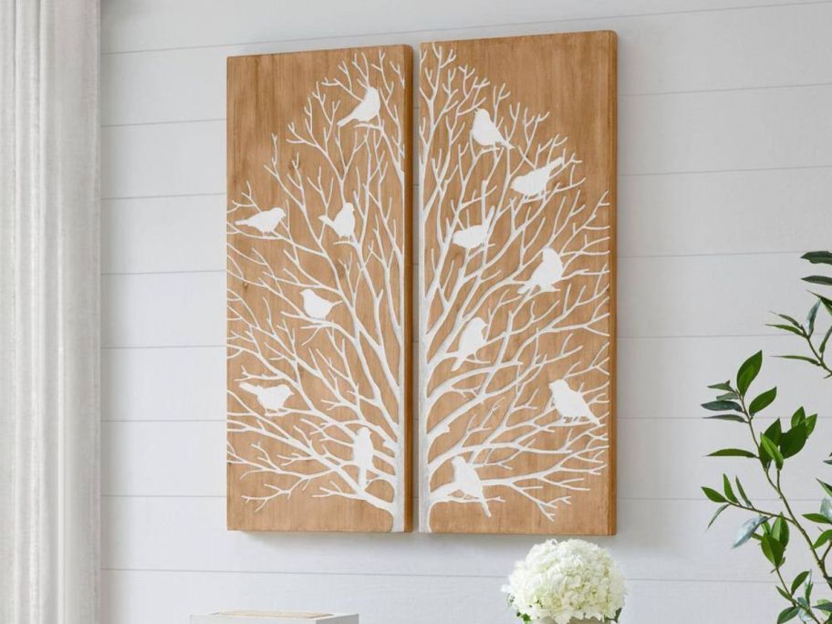 Two wooden panels on a wall depicting a tree with birds